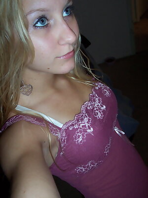a young woman taking a selfie in a pink tank top and lace trimmings on her shirt and bottom half of her shirt is off to the and the side of her body, with her left side